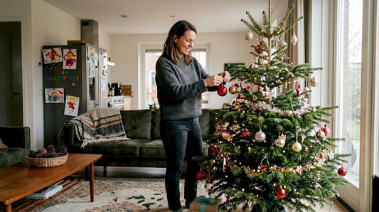 Een vrouw hangt een rode kerstbal in de kerstboom in de woonkamer.