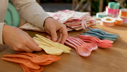 Een paar handen leggen herbruikbare plastic lepels netjes op tafel.